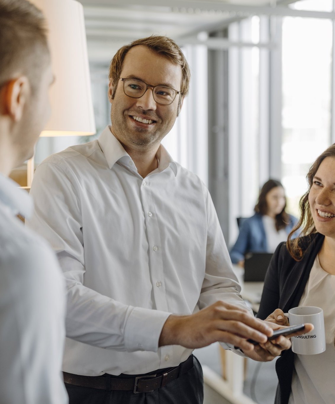 Ein Consultant zeigt zwei weiteren Consultants etwas auf seinem Smartphone.