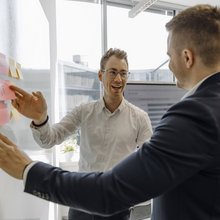 Zwei Consultants unterhalten sich über Post-Its an einem Whiteboard.