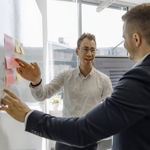 Zwei Consultants unterhalten sich über Post-Its an einem Whiteboard.