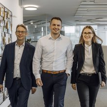 Drei Consultants laufen nebeneinander durch das Büro auf die Kamera zu.