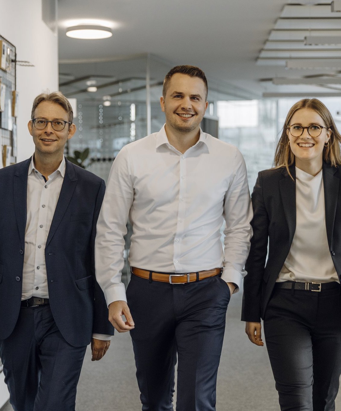 Drei Consultants gehen im Büro an einer kreativen Wand vorbei.